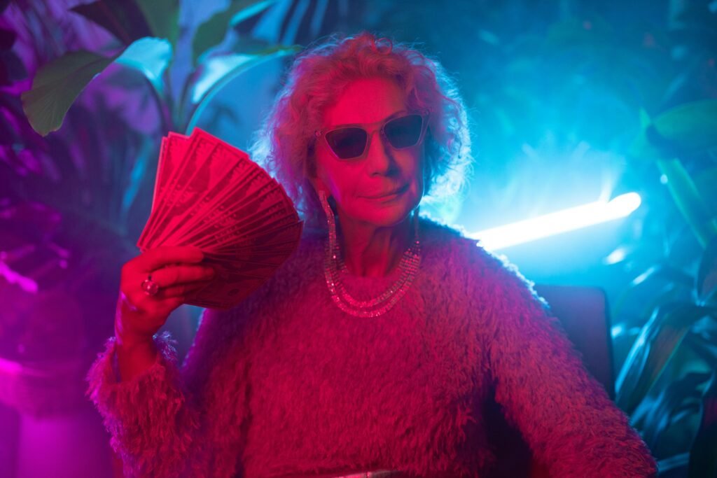 An elderly woman exudes confidence and style under neon lights, holding a fan of cash.